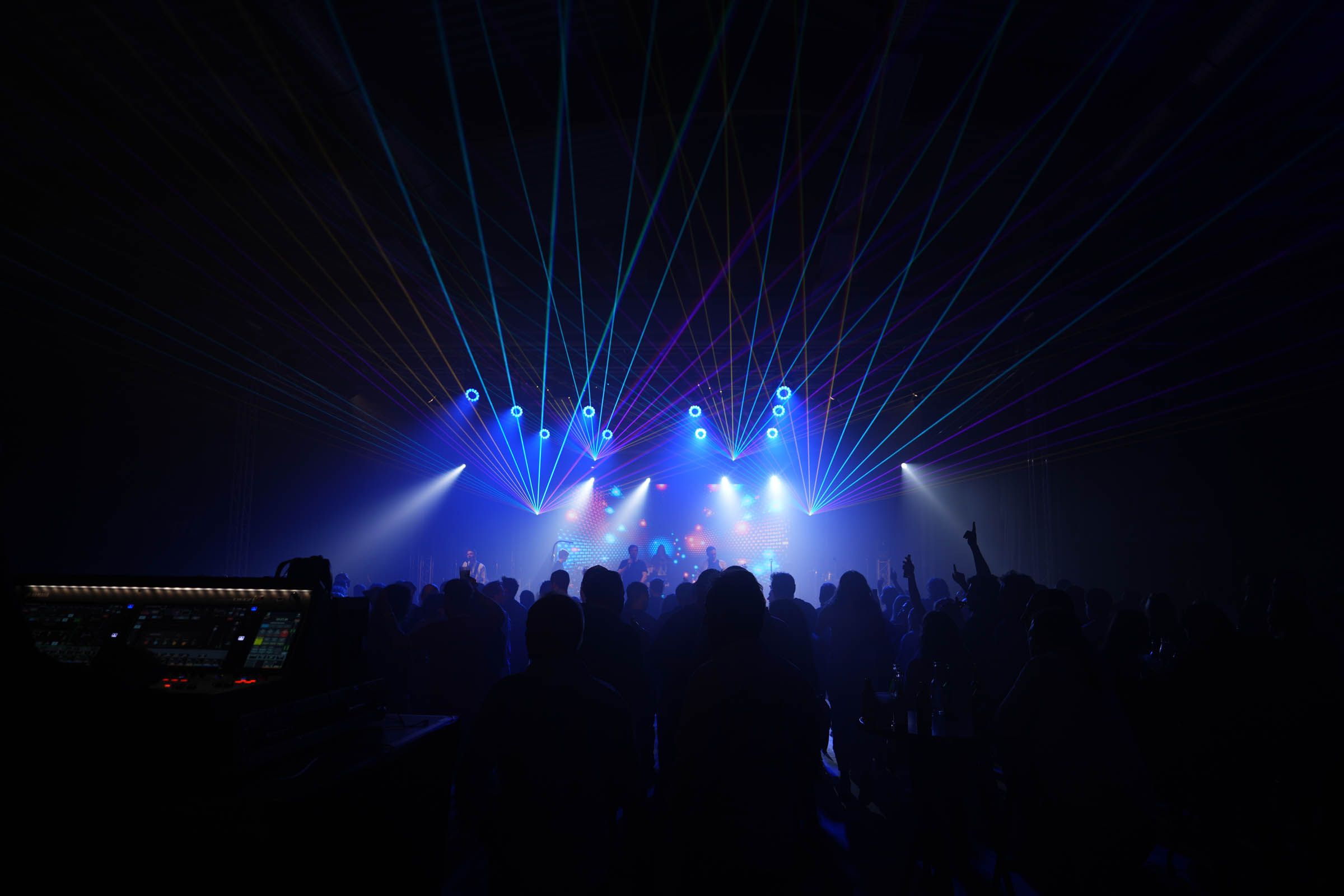 Menschenmenge vor einer Bühne mit bunten Laserstrahlen und Bühnenlichtern